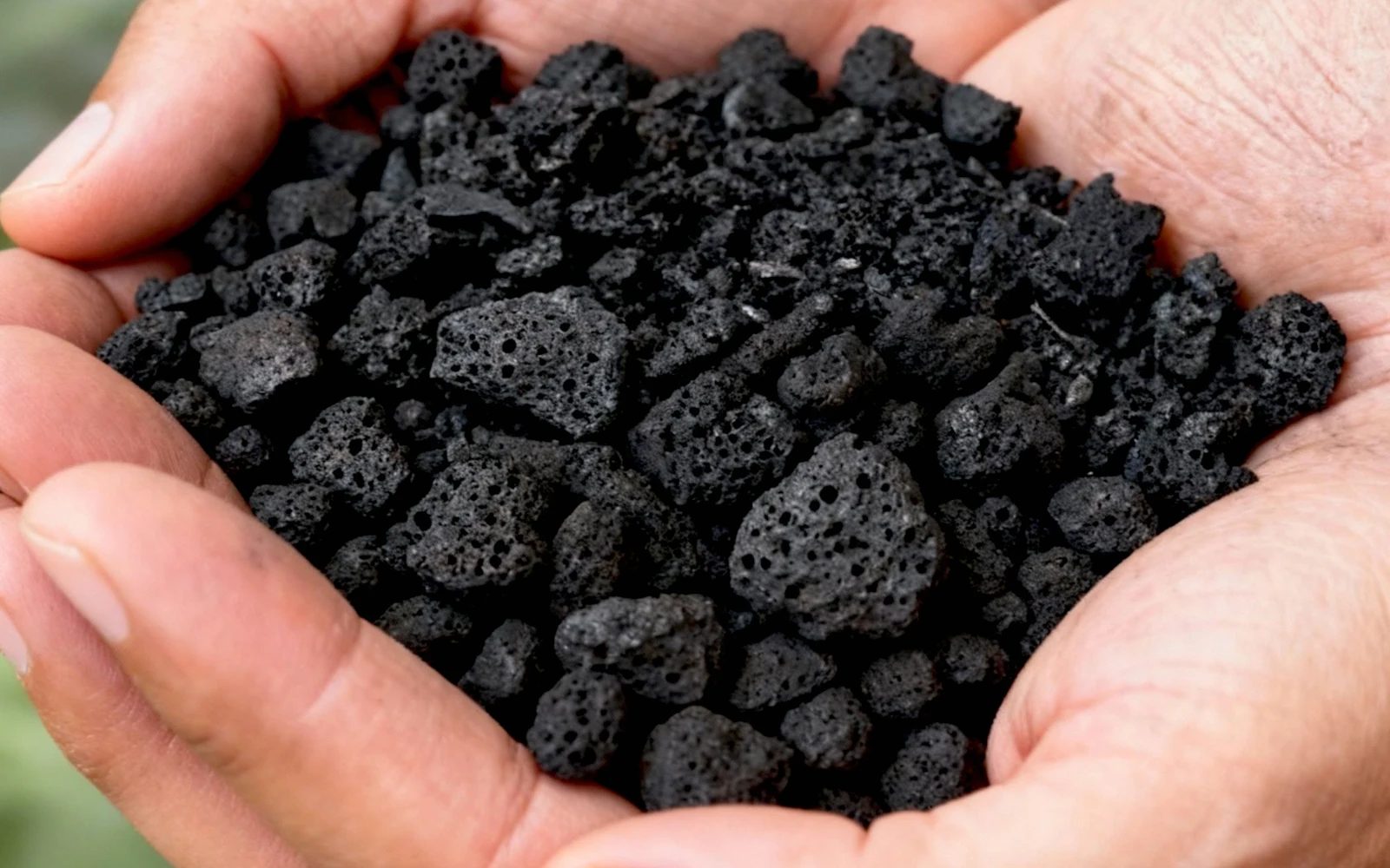 Biochar beziehungsweise Biokohle als Granulat in den Händen, symbolisch für Spezifikation und Projektfähigkeit.